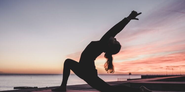 Frau praktiziert Yoga im Lotussitz, umgeben von Natur - Darstellung der ganzheitlichen Wirkung von Yoga auf die Gesundheit